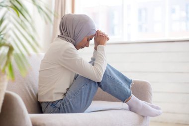 Tesettürlü genç Müslüman bir kadın kanepede bağdaş kurarak oturur, kafasını düşünceli bir şekilde ellerine yaslar, depresyon, stres ve kayıp yaşar. Boşanma, savaş. Mülteci gözlerini kapattı ve dua etti..