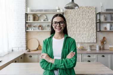 Genç bir kadının portresi, kızım. Öğrenci, evde mutfakta serbest çalışan, kollarını göğsünde kavuşturmuş, güvenle ve gülümseyerek kameraya bakıyor..