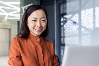 Genç, güzel ve başarılı iş kadını ofis içinde çalışan Asyalı finansör, gülümseyen ve dizüstü bilgisayara bakan kadın programcı stajyer öğrenci,.