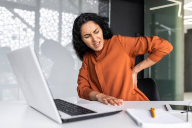 Ofis çalışanı Latin Amerikalı iş adamı iş yerinde hasta, aşırı yorgun bir iş kadını sırt ağrısı çekiyor, elleriyle sırtına masaj yapıyor.