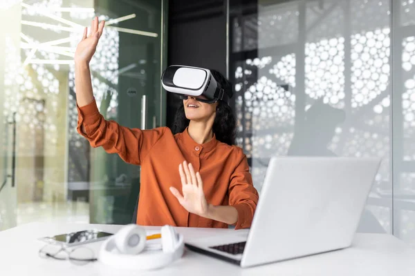 stock image Young successful woman inside the office using vr glasses, virtual reality simulator cross charts and documents online, latin american woman using laptop at work.