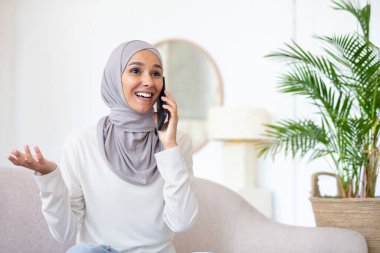 Genç Arap kadın tesettürde oturuyor ve telefonda konuşuyordu. El hareketleriyle. Gülümsüyor.