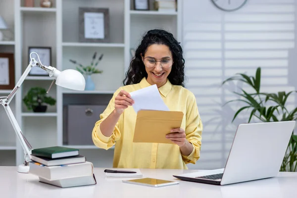 Successful and happy hispanic businesswoman working remotely at home, woman received good news notification mail reading and happy, working sitting at table with laptop.