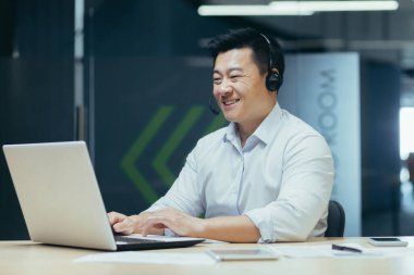 Ofiste kulaklıkla çalışan gülümseyen Asyalı genç bir adamın portresi..