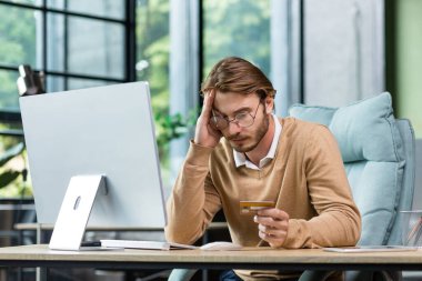 Ofiste çalışan dolandırılmış ve hayal kırıklığına uğramış bir işadamı, elinde banka kartı olan bir adam ve çevrimiçi mağazadan satın almaya çalışan bir adam, online dolandırıcılık ve aldatmaca.