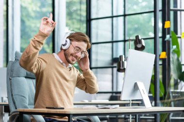 Gözlüklü bir işadamı kulaklıkla müzik dinler, işyerinde dinlenirken dans eden bir adam, işte dizüstü bilgisayar kullanır.