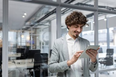 İyi sonuçlardan memnun olan işadamı ofis içinde çalışırken gülümser ve tablet bilgisayarını tutar, finans alanında iyi başarılar elde eder..