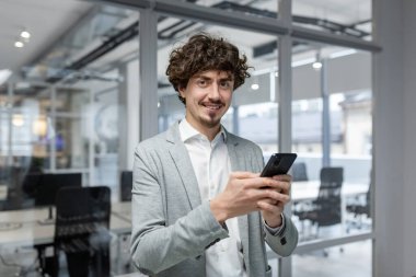 Başarılı bir iş adamı portresi, sakallı bir adam gülümseyen ve kameraya bakan, ofis içinde takım elbiseli bir patron akıllı telefon tutuyor.