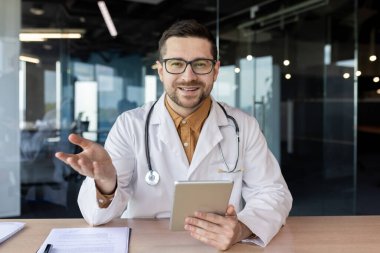 İnternetten bir doktora danışıyorum. Genç bir erkek doktor masadaki ofiste oturur ve hastayla görüntülü konuşma yapar. Gülümser ve kameraya tavsiye verir..