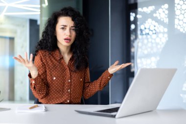 Frustrated and sad woman inside office looking at camera, businesswoman unhappy with achievement results working at desk using laptop at work. clipart