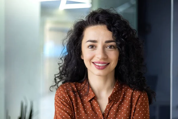 stock image Close up photo portrait of beautiful Latin American woman with curly hair , businesswoman inside office building smiling and looking at camera.