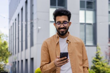 Genç Hindu programcı bir mühendis ofis binasının önünde yürüyor, bir işadamı telefonu tutuyor ve bir mesaj yazıyor, gömlek ve gözlüklü bir adam gülümsüyor ve sosyal medyada geziniyor.