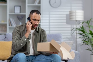 Evde sinirli bir Afrikalı Amerikalı genç teslimat servisiyle telefonda konuşuyor, paketle ilgili sorunları çözüyor. Elinde tuttuğu açık kutuya hayal kırıklığına uğramış gibi bakıyor..