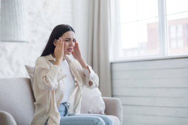Evdeki kanepede oturan ve elleriyle başını tutan genç bir kadının portresi. Depresyon ve zihinsel bozukluklardan muzdarip, şiddetli baş ağrısı ve stres hissediyor. İntihar etmeyi düşünüyorum..