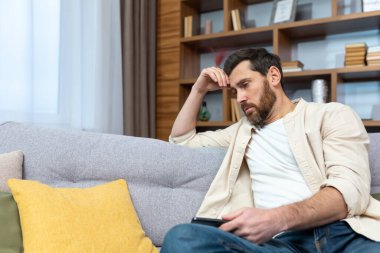 Üzgün, depresyondaki olgun bir adam evde, kanepede tek başına oturuyor..