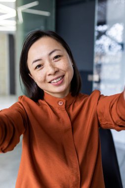 Dikey çekim, ofis Asyalı iş kadınından video görüşmesi modern ofis binasında çalışıyor arkadaşlarıyla uzaktan konuşma video görüşmesi için telefondaki uygulamayı kullanıyor..