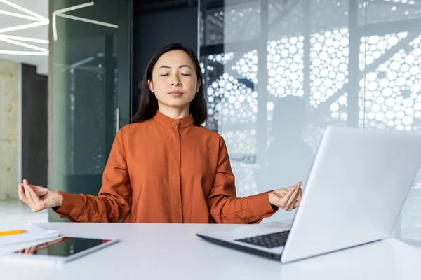 stock image Young beautiful Asian web developer working inside office building, woman resting meditating at workplace with eyes closed, female worker using laptop to write code