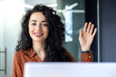 Online meeting video call young beautiful hispanic woman working in modern office, businesswoman using laptop to communicate with colleagues, female worker smiling and saying hello to web camera