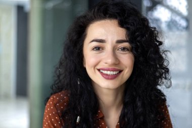 Close-up portrait of beautiful Latin American businesswoman smiling and looking at camera, working inside modern office.