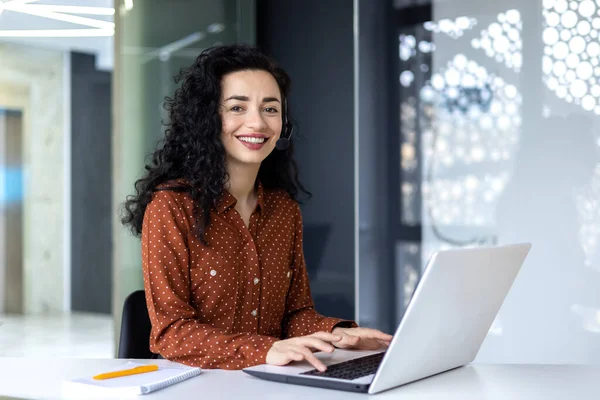 stock image Portrait of Latin American business woman, office worker looking at camera and smiling, using headset and laptop for remote online communication, customer support tech call center worker.