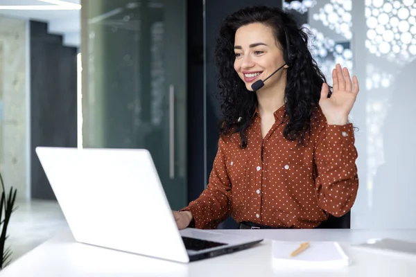 Video call online meeting with colleagues, Hispanic woman working inside modern office, businesswoman smiling and talking remotely using laptop and headset.