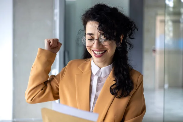 Happy hispanic business woman received letter from bank notification in envelope, happy business woman reading and reaching for good news, working inside office.