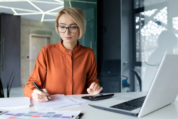 stock image Serious successful businesswoman behind paper work inside office, financial worker thinking about bills and reports, working at workplace with papers using laptop.