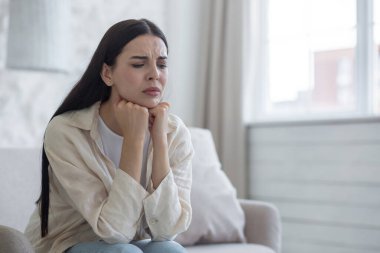 Evdeki kanepede oturan üzgün genç kadın, gözleri kapalı, elleri birbirine kenetlenmiş. Depresyon geçiriyor, ağlıyor, sorunları çözmeyi düşünüyor..