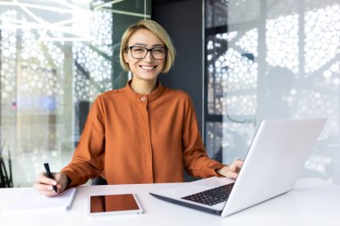 Ofis içinde evrak ve dizüstü bilgisayarla çalışan iş kadını, çalışan evrak işleri mali göstergelerin gülümsediğini ve başarı ve çalışmanın sonuçlarından mutlu olduğunu hesaplıyor..