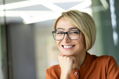 İş yerindeki güzel sarışın iş kadınının yakın plan fotoğrafı. Gözlüklü kadın, gülümsüyor ve kameraya bakıyor. Mutlu kadın portresi.