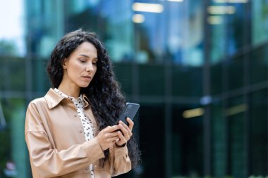 Elinde telefonla ciddi bir iş kadını, mesaj yazmayı ve haberleri okumayı düşünen Latin Amerikalı bir kadın, ofis binasının önünde yürürken akıllı telefon uygulaması kullanan bir patron..