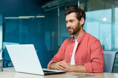 Ofis içinde dizüstü bilgisayarda çalışan yetişkin bir iş adamı. Programcı gülümsüyor. Yazılım kodlarını okuyor ve kontrol ediyor..