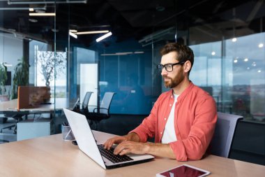 Düşünen ve ciddi bir adam ofis içinde dizüstü bilgisayarla çalışıyor, odaklanmış programcı yeni yazılım kodluyor..