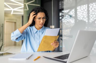 Üzgün ve üzgün iş kadını, kötü haber, finansal borç içeren bir mektup iletisi aldı. Ofis içinde dizüstü bilgisayarla çalışan, haber okuyan depresif İspanyol kadın..