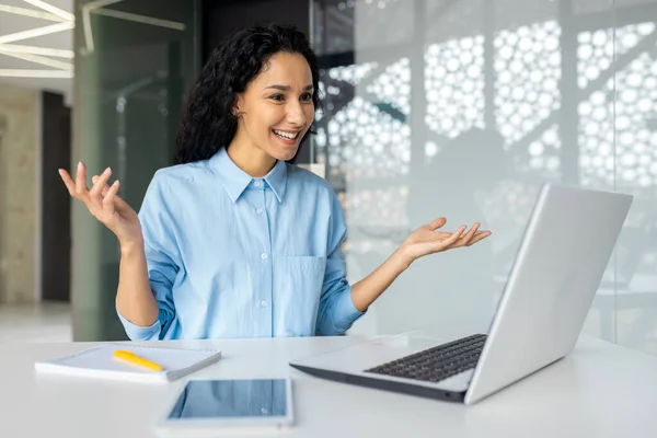 stock image Smiling and successful business woman talking remotely using laptop for video call, Hispanic woman smiling at workplace chatting with colleagues online, business meeting remote.