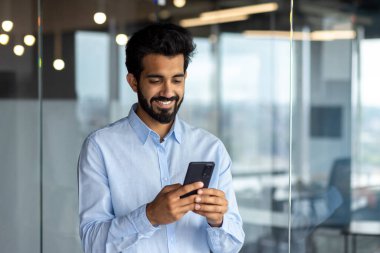 Genç ve başarılı bir iş adamı telefon kullanıyor, elinde akıllı telefon uygulaması kullanıcısı, gülümsüyor internette geziniyor ve arama yapıyor..