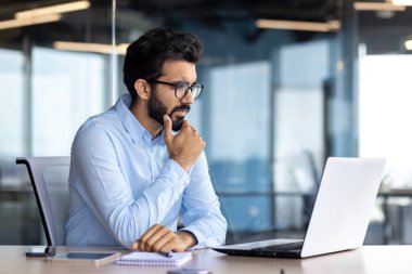 Ciddi düşünen iş adamı iş yerinde, tişörtlü olgun Hintli adam dizüstü bilgisayarda çalışıyor, gözlüklü programcı teknik sorunları çözmeyi düşünüyor..