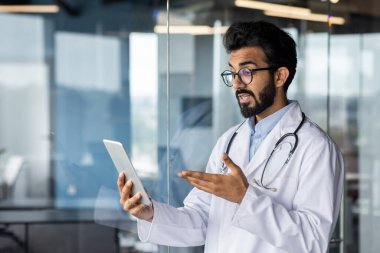 Modern klinikte başarılı bir Hintli doktor. Uzaktan kumandalı hastalara danışmanlık yapıyor. Video görüşmesi için tablet bilgisayar kullanıyor..