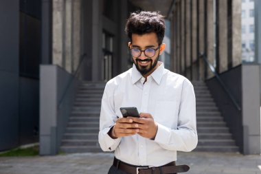 Yakın plan iş adamı şehri geziyor ve akıllı telefondan başvuru yapıyor. Elinde telefon tutan gülümseyen İspanyol bir adam internet sayfalarına göz atıyor, mesajlar yazıyor ve online mağazada seçim yapıyor..