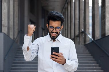 Ofis binasının önünde yürüyen Hintli bir adam, bir işadamına online bir galibiyet mesajı geldi, elini tutan bir adam zafer ve zafer jesti..