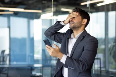 Üzgün ve hayal kırıklığına uğramış bir adam internette kötü haber okuyor. Akıllı telefondaki uygulamayı kullanıyor. İş yerindeki depresif iş adamı..