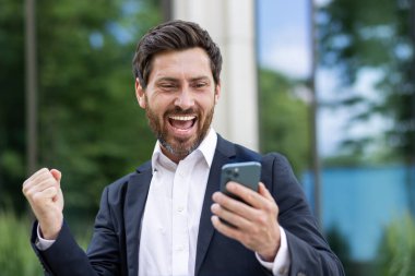 Yetişkin bir iş adamı telefonla zaferi kutluyor. Takım elbiseli patron internette iyi bir bilgilendirme aldı. Ofis binası dışında el ele tutuşan biri..
