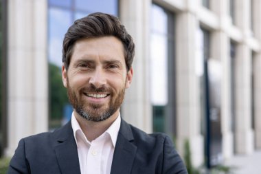 Patron kameraya bakıyor ve gülümsüyor, sakallı genç bir bankacı ve yakın plan portresi var..