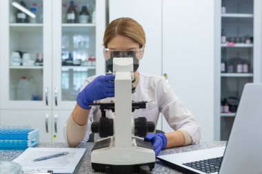 Laboratuvarda mikroskopla çalışan ciddi ve odaklanmış kadın araştırmacı olgun ve deneyimli bir bilim adamı tıp eğitimi alıyor ve test ediyor..