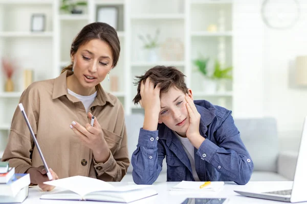 Cute and boring study at home, mom explains homework to son, family study at home sitting in living room, son doesnt understand homework upset and bored.