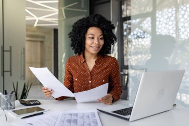 Genç başarılı finansör ofis içinde belge ve sözleşmelerle çalışır, mali faaliyetlerin sonuçlarından tatmin olur, iş kadını hesapları, raporlar ve sözleşmeler, dizüstü bilgisayarlar.
