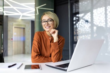 İş yerindeki genç ve güzel bir iş kadınının portresi. Kadın işçi gülümseyen bir dizüstü bilgisayar kullanıyor ve kameraya bakıyor..