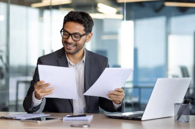 Kağıt işlerinde başarılı, olgun, deneyimli bir finansör, finansal başarıların sonuçlarından memnun bir Arap gülümsemesi, sözleşmeleri gözden geçirme, faturalar ve hesaplarla ilgili açıklamalar, takım elbiseli bir işadamı..