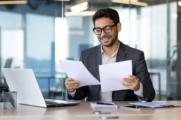 stock image Successful mature experienced financier on paper work, Arab smiling satisfied with results of financial achievement, reviewing contracts, invoices and statements with accounts, businessman in suit.