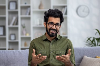 İnternetten video görüşmesi, evdeki koltukta oturan Hintli adam, web kamerasına bakıp gülümsüyor ve meslektaşlarıyla uzaktan konuşuyor..